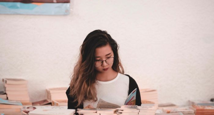 young Asian woman reading a book around tables filled with books