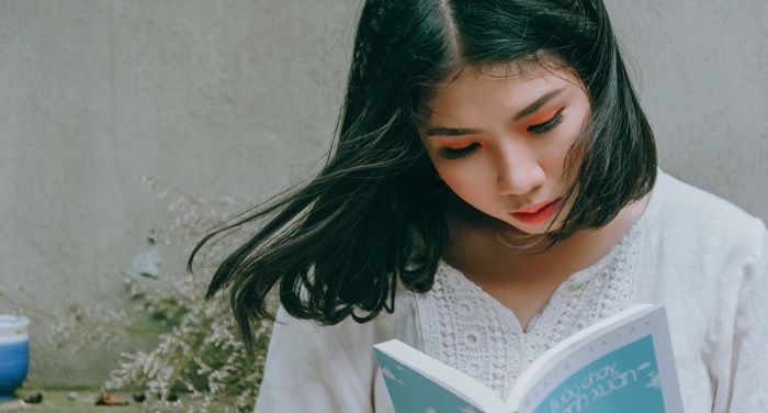 Asian woman reading a book; she has orange eyeshadow on