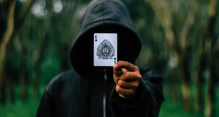 a photo of a hooded figure holding up an ace of spades in front of their face