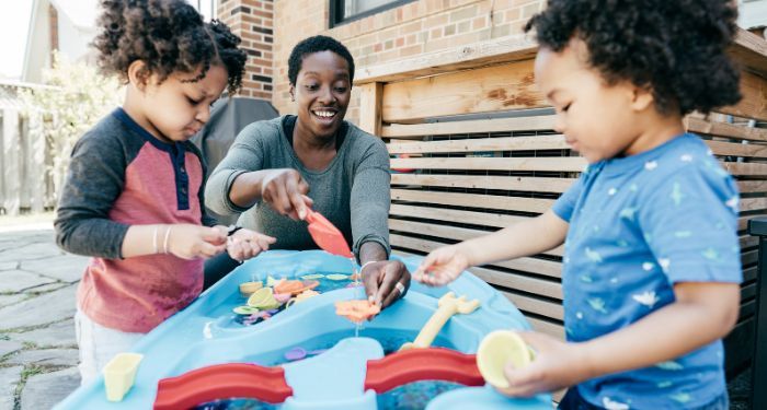 Image of an adult with two Black children playing at a water table