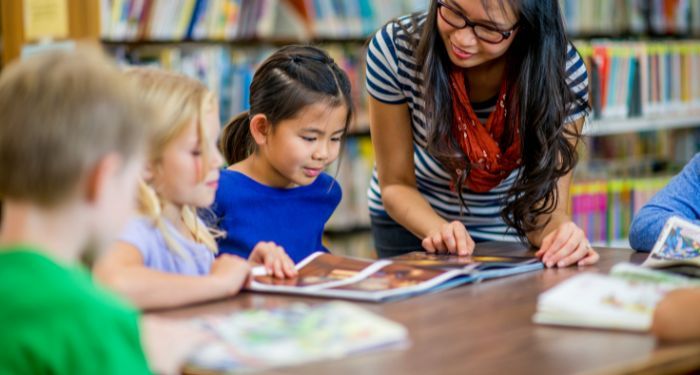 An Asian woman teaching elementary children in a library