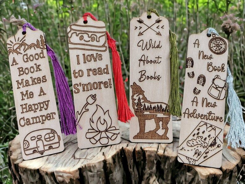 Four wooden bookmarks engraved with campers and tents with the sayings: "A good book makes me a happy camper," "I love to read 'smore," "Wild about books," and "A new book, a new adventure"