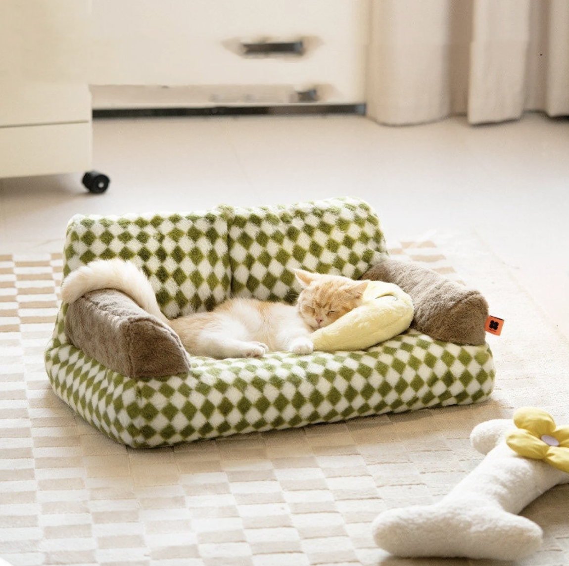 A blondish cat snoozes on a tiny green and white checkered couch shaped bed