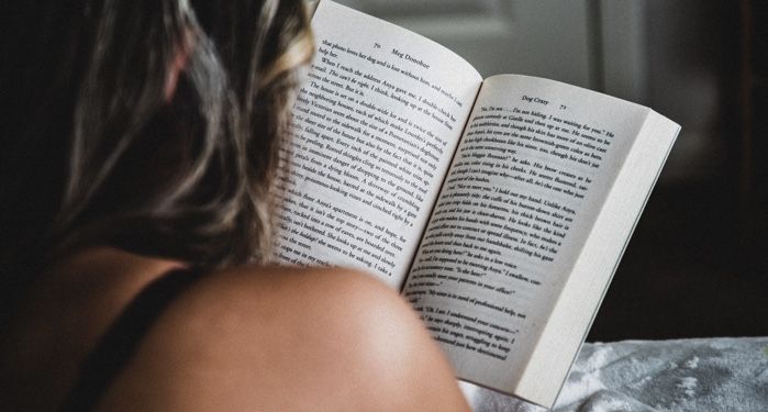 a person with long dark hair and a tanned shoulder reading a book