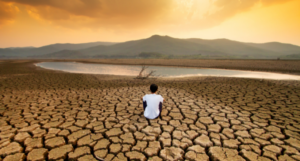 a photo of a someone sitting on a dried out, cracked lake bed watching the sun set