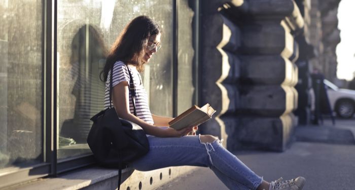 fair skinned woman of color sitting near a window with a book and smiling