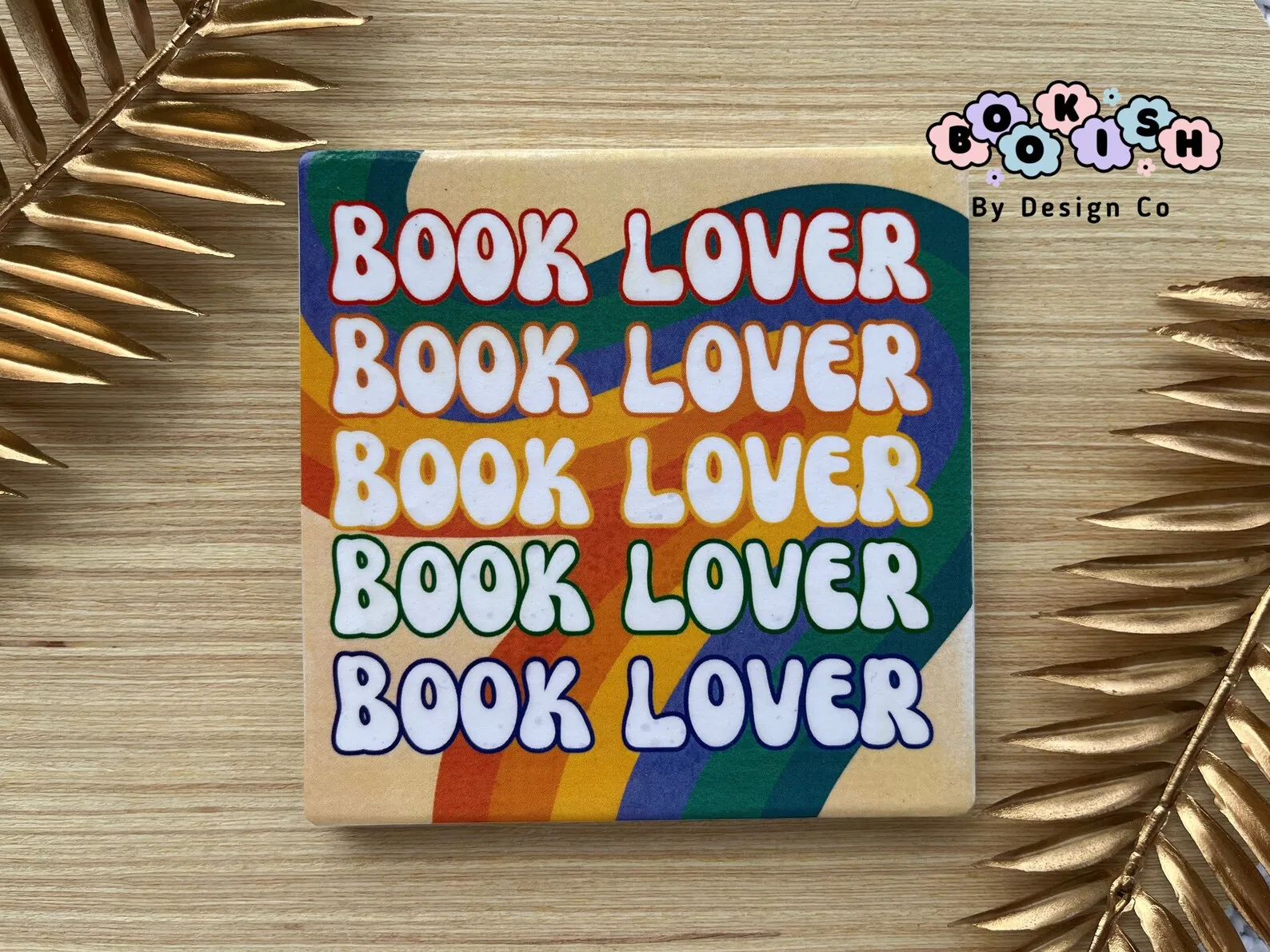 Book Lover Tile Coaster on a wooden table with golden leaves.