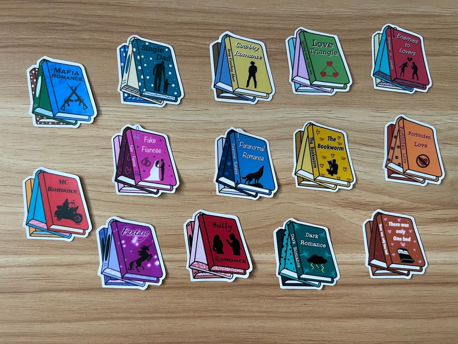 A set of 14 stickers on a wooden table with book tropes on them.