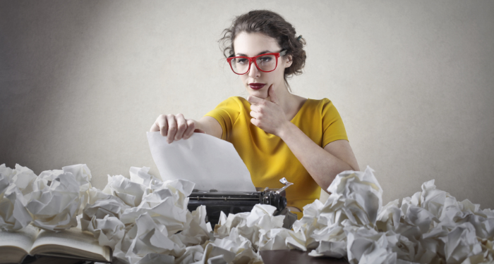 a photo of a woman writing at a typewriter surrounded by crumpled paper