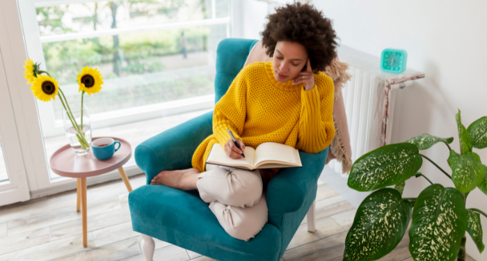 a photo of a Black woman sitting in an armchair and writing in a notebook