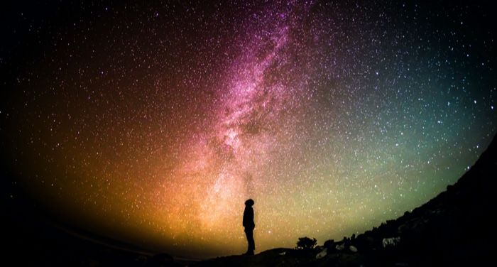 a person lookiing up at the night sky against a back drop of a starry sky