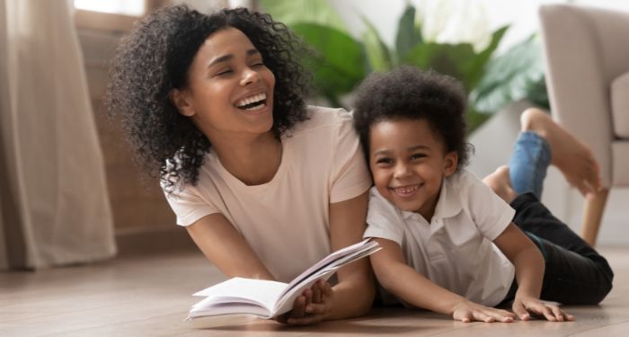 Black adult and child reading a book and laughing