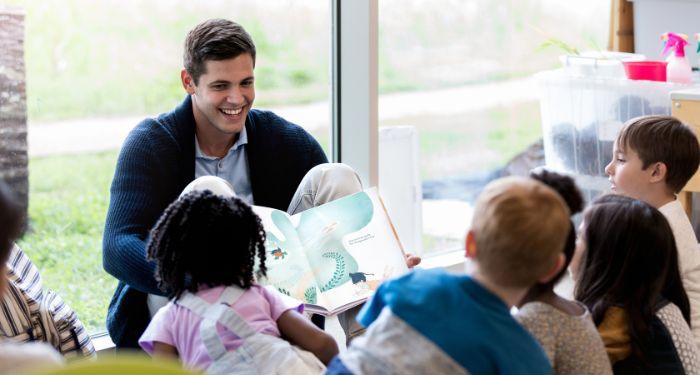 a man reading a picture book to a group of small children