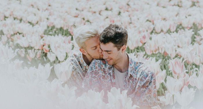 two white gay men nuzzling in a field of flowers