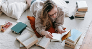 a photo of a white woman reading on the floor surrounded by stacks of books