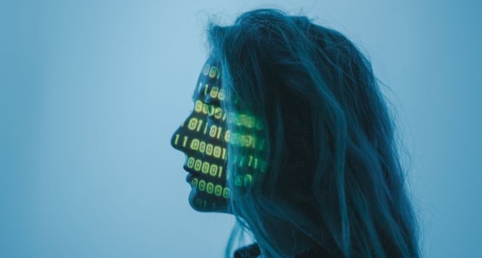 white woman with straight hair and a computer code displayed on her face with a projector