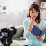 Person reading a book while filming themself with a camera