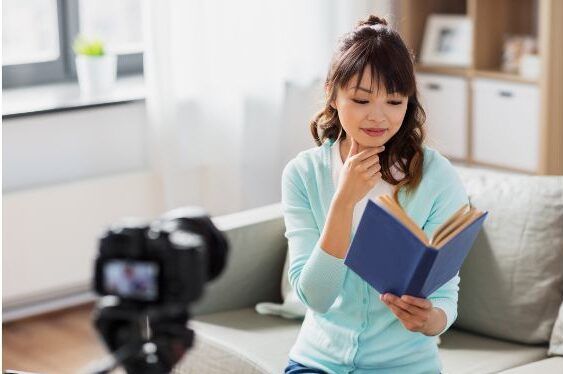 Person reading a book while filming themself with a camera