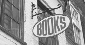 black and white image of a metal sign that says "books" hanging from the outside of a building