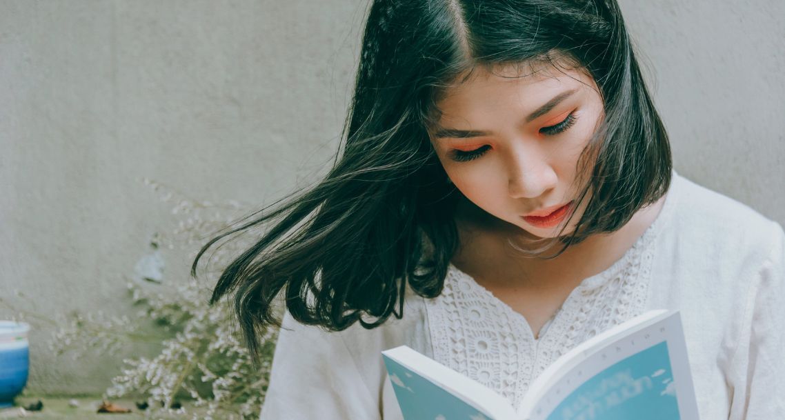 light-skinned Asian woman with orange eyeshadow and a bob haircut reading a book