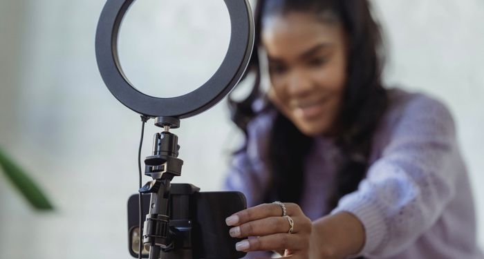 brown-skinned Black woman with long, curly hair adjusting a phone to record content