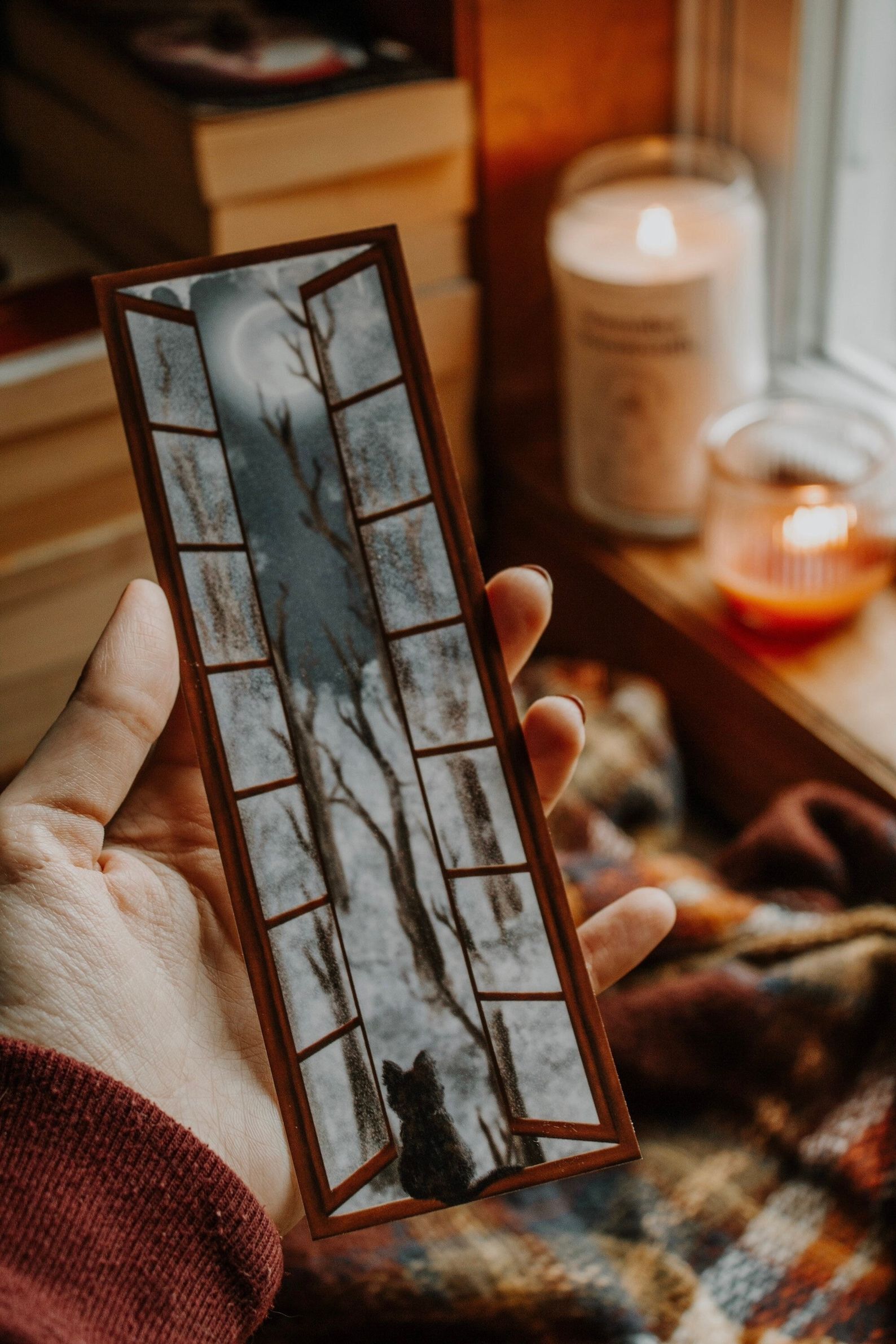 A bookmark depicting a window looking out on a winter scene at night, and a cat peering out