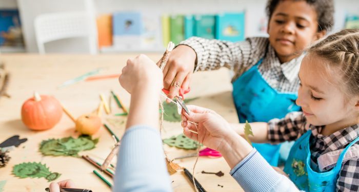 kids sitting at a table making crafts at a large table with bookshelves behind them