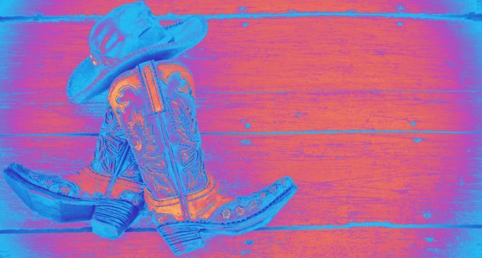 a cowboy hat and cowboy boots against a wood slab background. a nrigh neon blue, pink, and orange filter is applied to the entire image