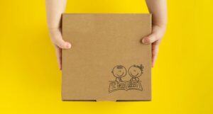 a child's hands holding a cardboard box with the graphic of two kids reading on the front of the box