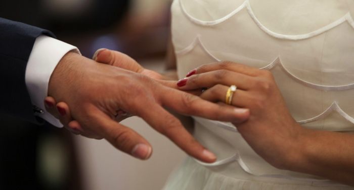 tan-skinned hands slipping on a wedding ring on another hand