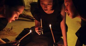 three lighter-skinned Asian women lighting candles in a ceremony