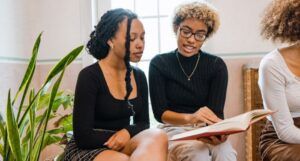 two light-skinned Black women discussing a book