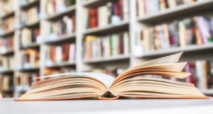 an open book on a table with bookshelves out of focus in the background