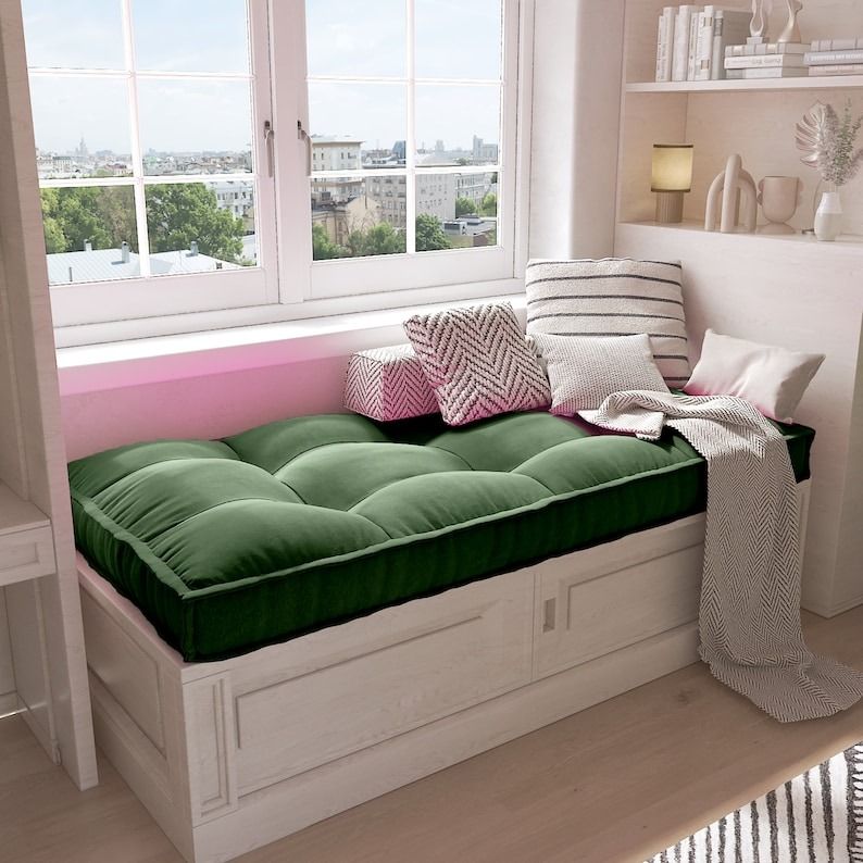 a bench with a cushion by a window, with bookshelves behind