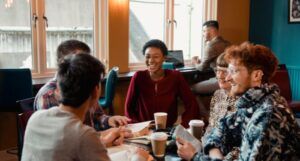 a group of diverse people gathered 'round a table full of coffee cups and books