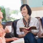 three women of different skin tones and races sitting, smiling, and discussing books