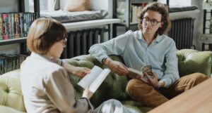 two people talking on a couch, both holding books