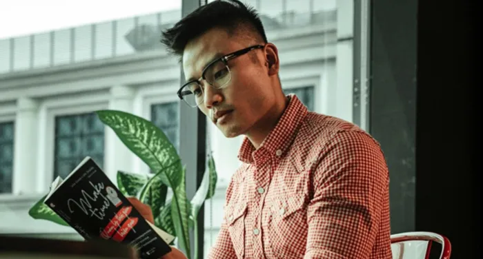 medium skin toned Asian man reading a book in a cafe
