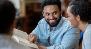 a light brown-skinned man smiling and discussing a book with tan-skinned woman