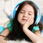 a photo of a kid with light skin and long hair closing their eyes, listening to headphones