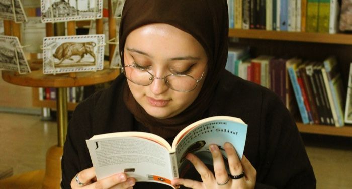 light medium skinned woman of color wearing a hijab and reading a book in a bookstore