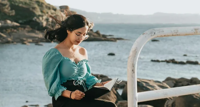 a woman reading by a rocky shoreline