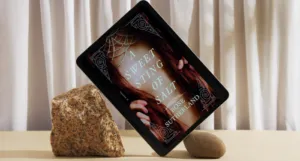 a photo of a tablet propped up on rocks displaying the cover of A Sweet Sting of Salt