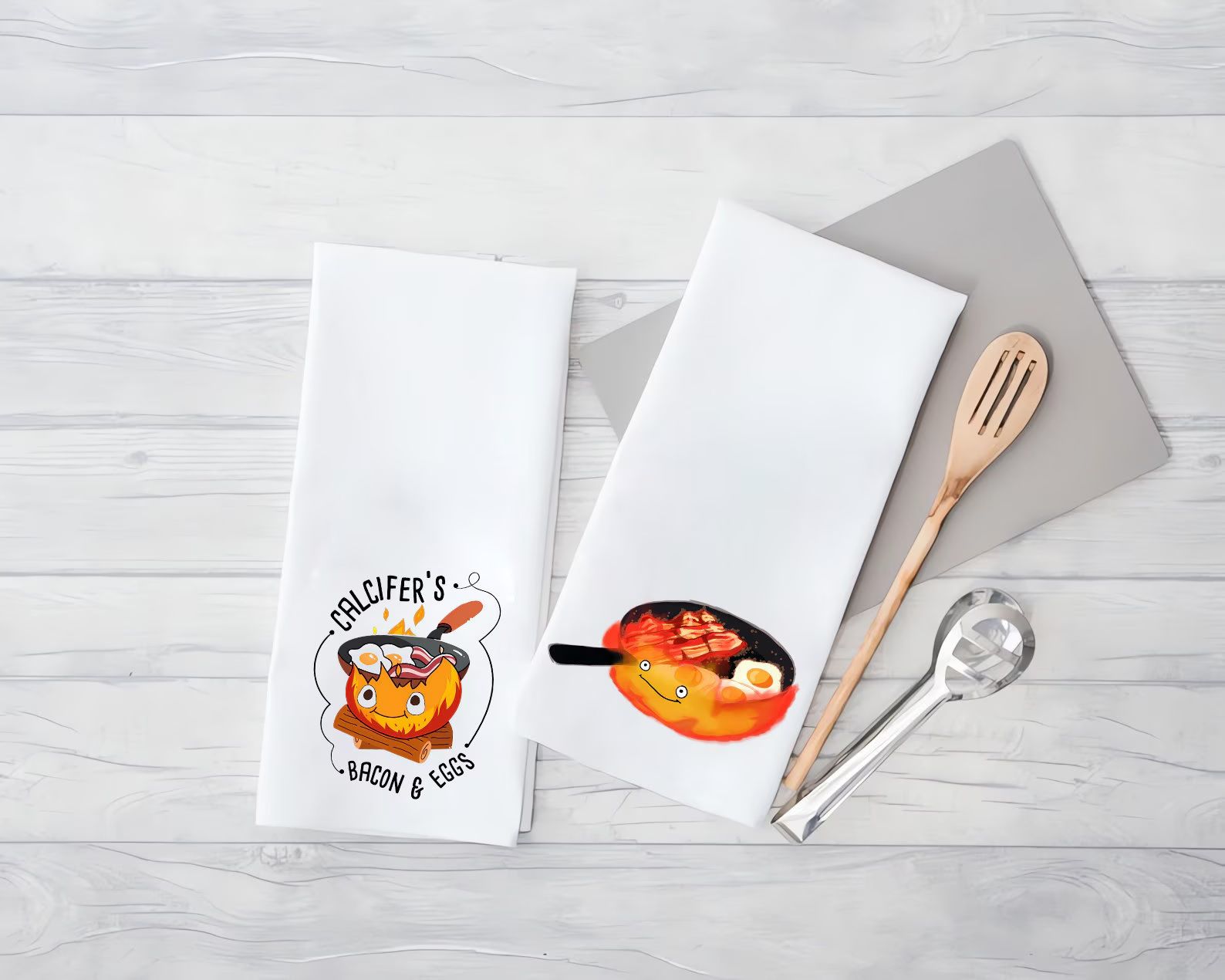 Two white tea towels featuring Calcifer from Howl's Moving Castle frying up bacon and eggs on a skillet