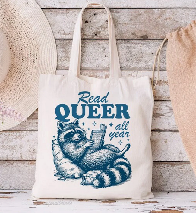 tote bag with an illustration of a raccoon reading that says read queer all year