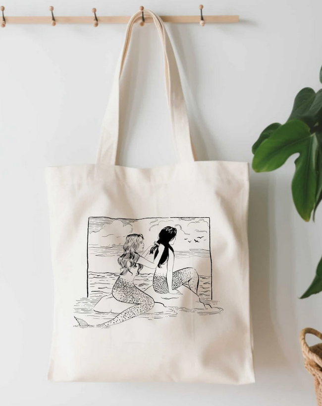 black and white sketch illustration on a tote bag of a mermaid brushing another mermaid's hair