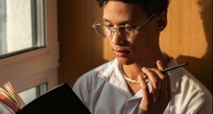 an Asian man with lightly tanned skin holding a pencil and reading a book