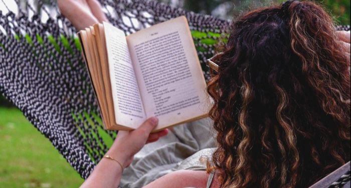 fair-skinned person with long, curly hair reading in a hammock outside