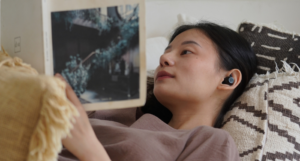 an Asian woman listening to earbuds while reading a book