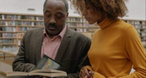 two Black people reading a book in a library